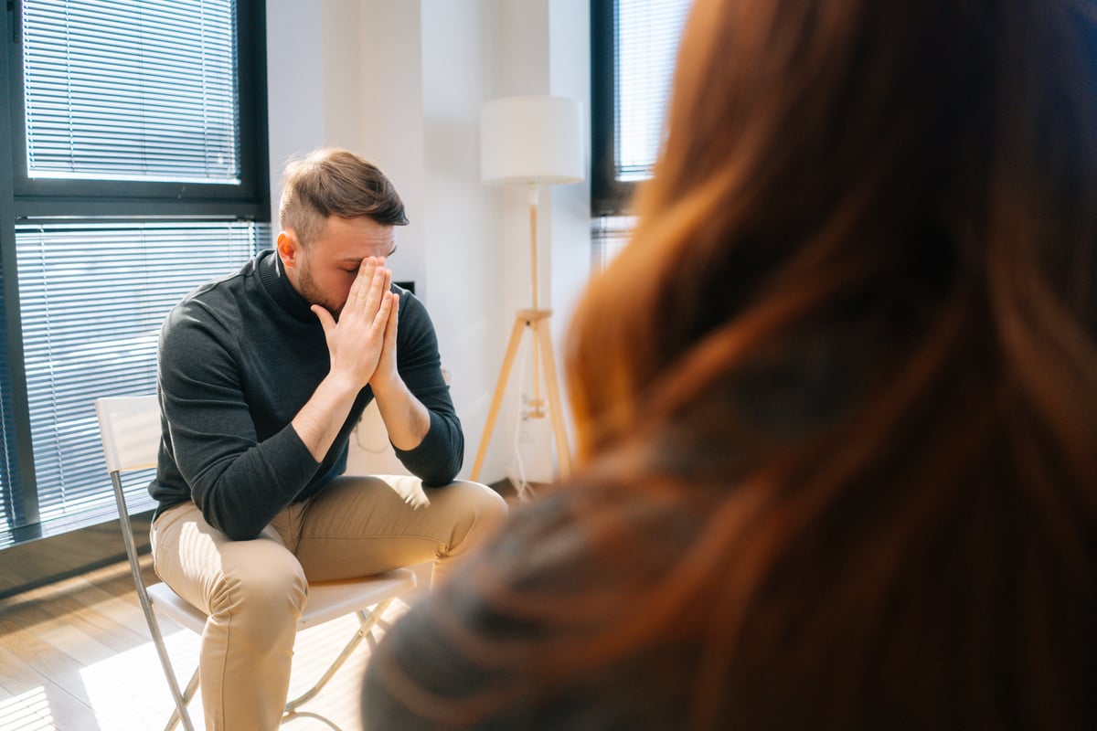 Sad depressed male talking with compassionate patients and psychotherapist sitting in circle during group interpersonal therapy session.